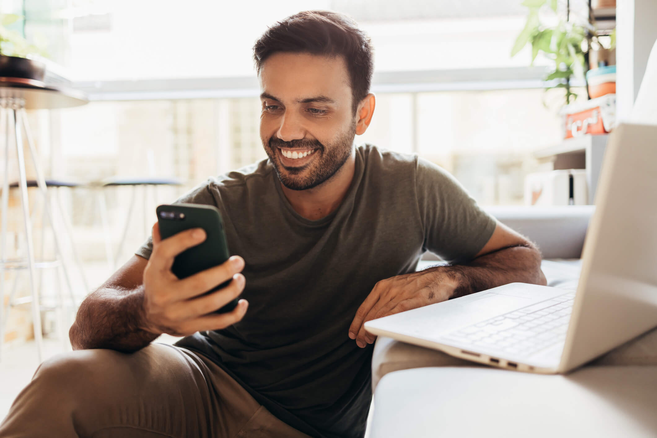 Young man smiling while looking at his phone sitting down on a couch.