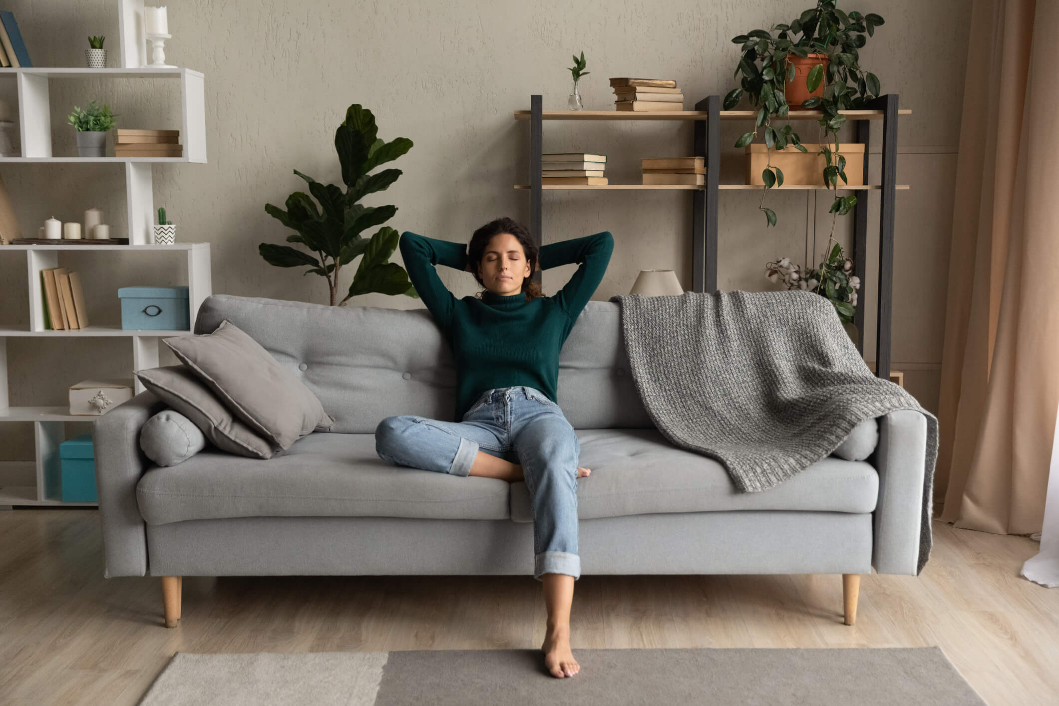 Young woman wearing a green sweater and jeans laying on a couch relaxed.
