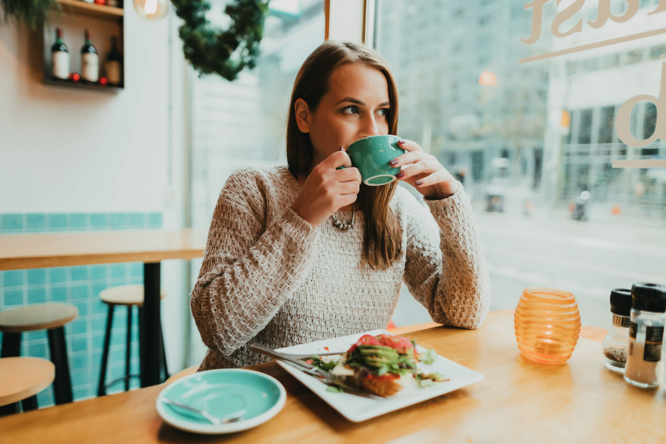 Young woman drinking coffee from a large green mug at a coffee shop.