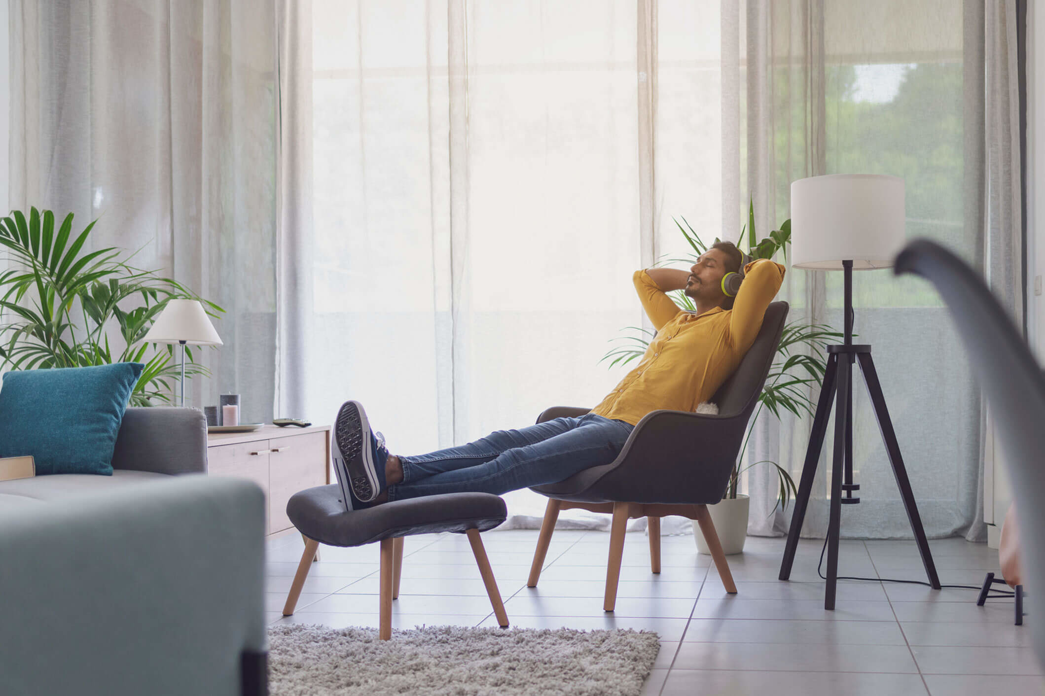 Young man in a yellow sweater and pants relaxing in a chair with his feet up and his hands behind his head.