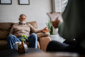 Image of a senior man talking with a psychotherapist during a therapy session at a clinic for PTSD treatment.