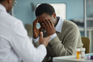 A young black man sits with his head in his hands while meeting with a specialist for anxiety disorders.