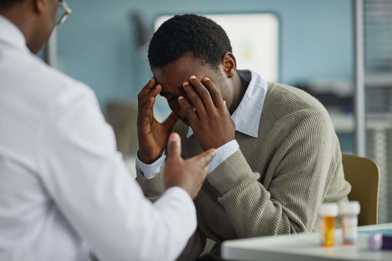 A young black man sits with his head in his hands while meeting with a specialist for anxiety disorders.