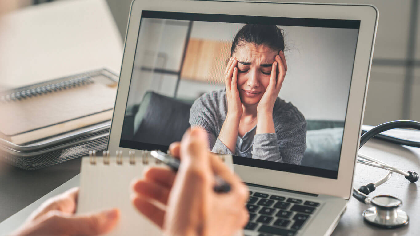 Female psychologist calms down emotional crying woman patient by video call during telehealth for anxiety care.