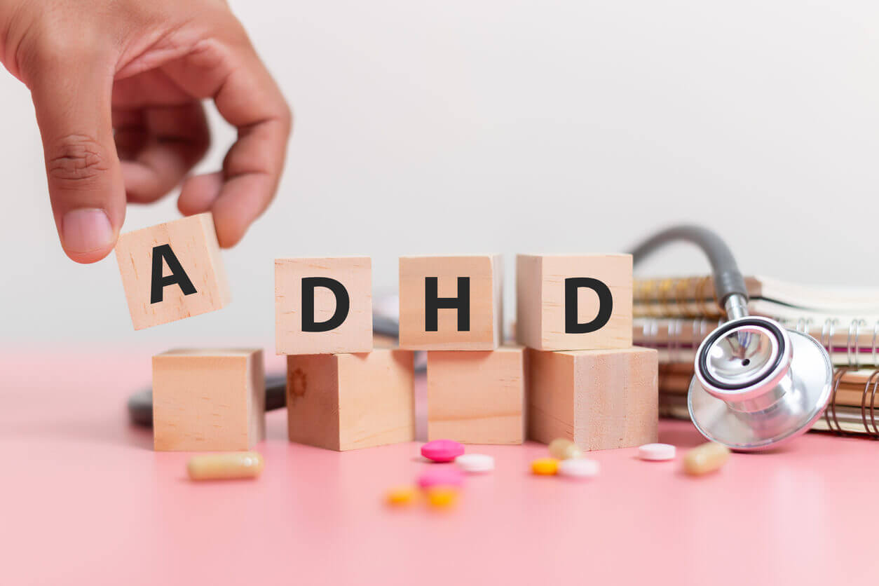 Hand holding wood cube block Abbreviation of ADHD with Stethoscope and pills on pink table.