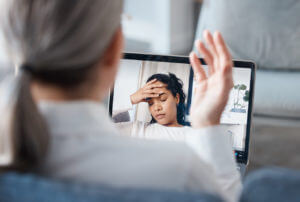 Image of a psychologist sitting and using a laptop for an online consultation with her depressive patient.