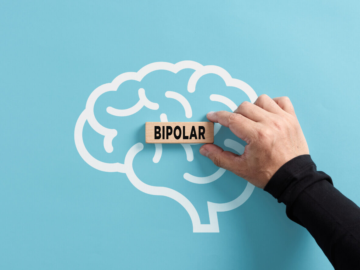A man hand puts a wooden block with the word bipolar on a human brain symbol